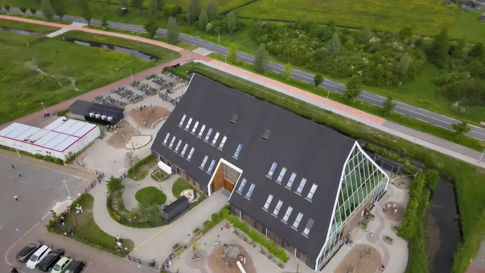 Luchtbeeld van een schoolgebouw met een glazen puntgevel, vanuit de drone.